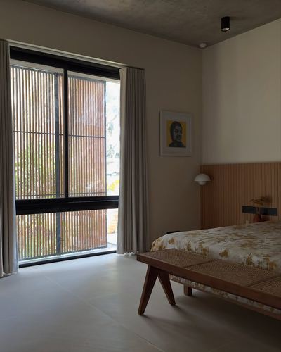 Bedroom with fluted wood headboard, cane bench, and tall louvered glass door opening to greenery.