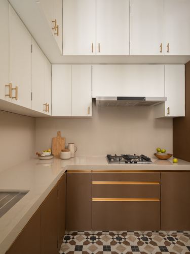 L-shaped kitchen with white upper cabinets, ribbed brown lower cabinets, brass handles, patterned floor tile