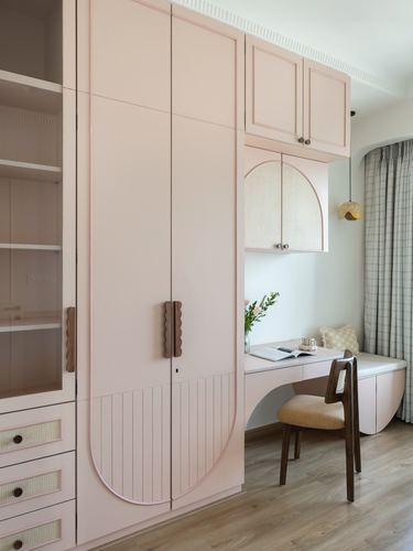 Blush pink fluted wardrobe with arched door beside a built-in study nook and window seat