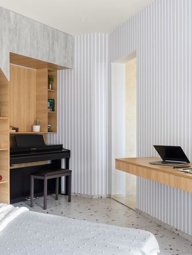 Bedroom corner with built-in wood shelving, upright piano, striped walls, and floating desk with laptop