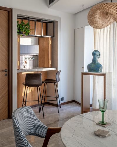 Dining nook with marble table, sculpture on console, and view into wood-slatted breakfast bar kitchen