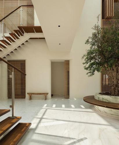 Double-height entry courtyard with floating staircase, lattice screens, and a large olive tree in a stone planter