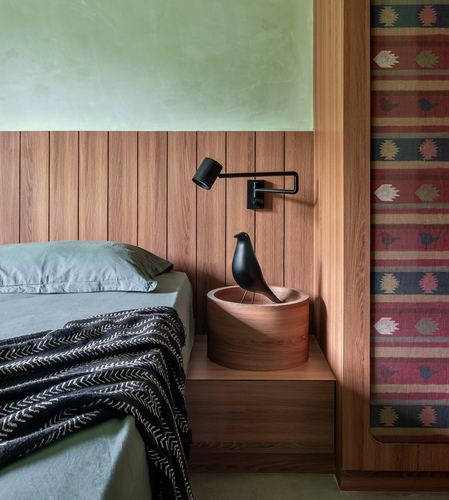 Bedside nook with wood panelling, wall lamp, wooden bird sculpture and kilim textile panel