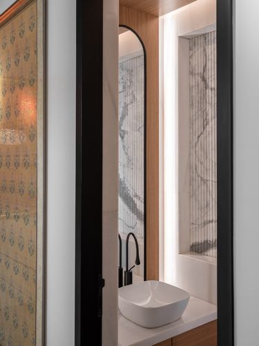 Doorway view into a marble and wood powder room with arched mirror and vessel sink