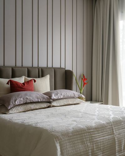 Bed with taupe channel-tufted headboard against fluted wall panelling, red heliconia flower on nightstand.