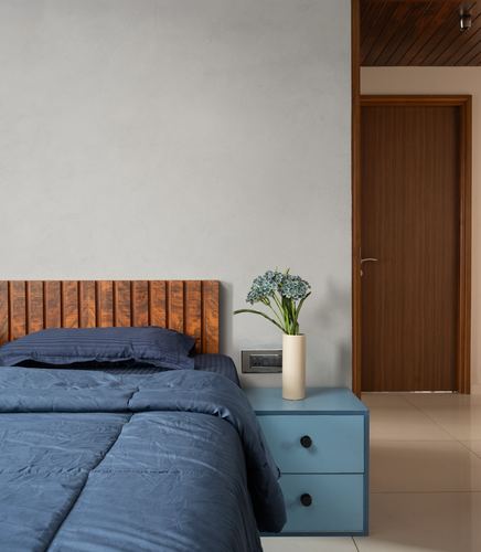 Bedroom corner with ribbed wood headboard, blue bedding, and blue bedside table beside an open wooden door