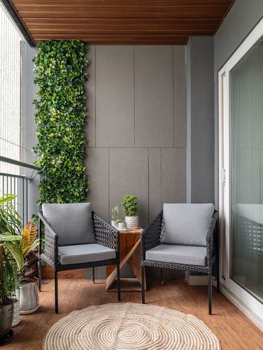 Balcony seating with two wicker chairs, wooden table, and a vertical green wall against grey panelled walls