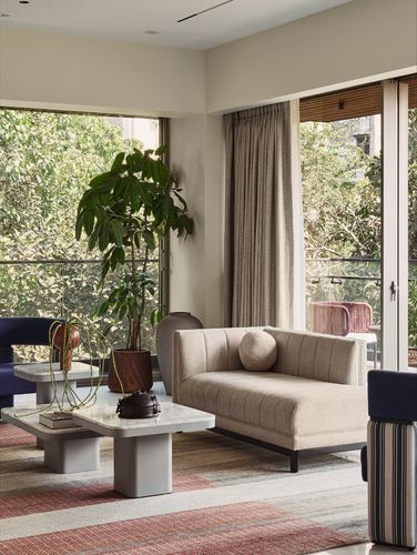 Beige chaise lounge and marble coffee tables in living room with floor-to-ceiling windows facing trees