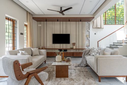 Beige living room with two sofas facing a wood-slat TV wall and open staircase behind
