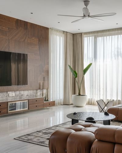 Living room with wood veneer TV wall, marble console, tan leather sofa and tall sheer-curtained windows