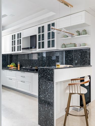 White kitchen with dark stone island, glass cabinets, and pendant light over bar seating