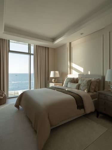 Beige hotel-style bedroom with floor-to-ceiling window overlooking the sea