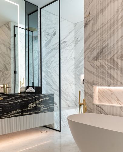 Marble bathroom with black stone vanity, glass shower partition, brass fixtures and oval freestanding tub