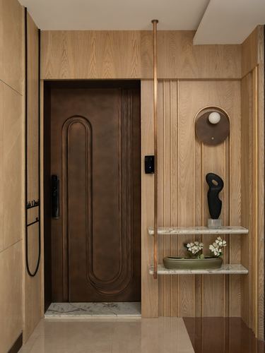 Foyer entrance with patinated copper door set in light wood veneer paneling and floating stone shelf
