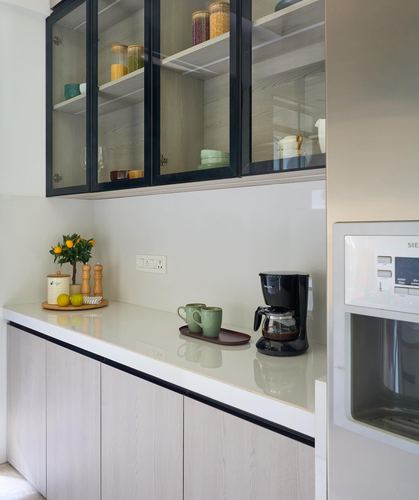 Modern kitchen counter with black-framed glass cabinets, coffee maker, and styled tray of mugs