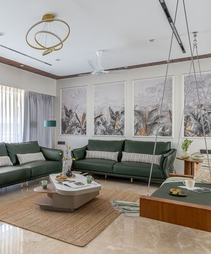 Green leather sofas around a sculptural coffee table beneath framed botanical wall art in a Vadodara living room