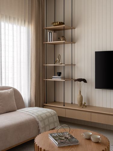 Beige living room corner with suspended wood shelving, tv, low console, and round coffee table