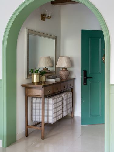 Entryway console with mirror and lamps seen through green arched doorway beside teal front door
