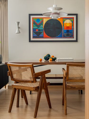 Dining nook with cane Pierre Jeanneret-style chairs, wood table, PH5 pendant and colorful abstract art
