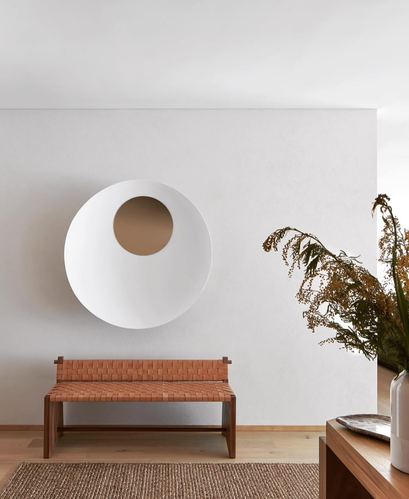 Woven leather bench under a round asymmetric mirror against a white plaster wall