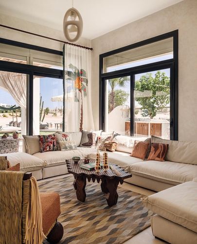 Sunlit living room with cream sectional, carved wood coffee table, patterned rug, and large windows to garden
