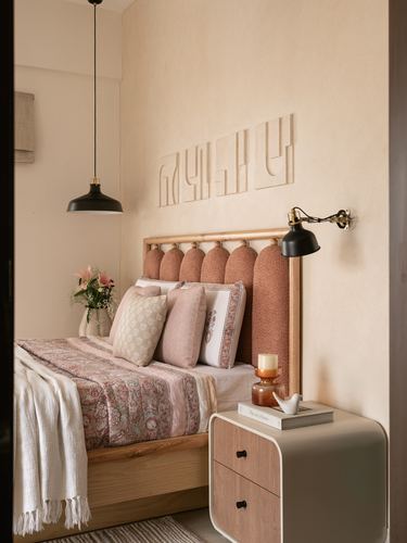 Bedroom with scalloped terracotta headboard, carved wall art, black sconce, and rounded bedside table
