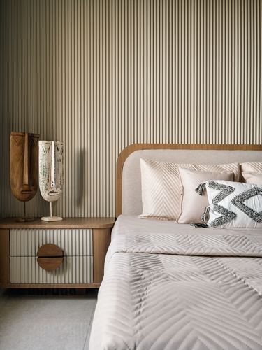 Bedroom corner with fluted wall panelling, curved headboard, and wooden mask decor on nightstand