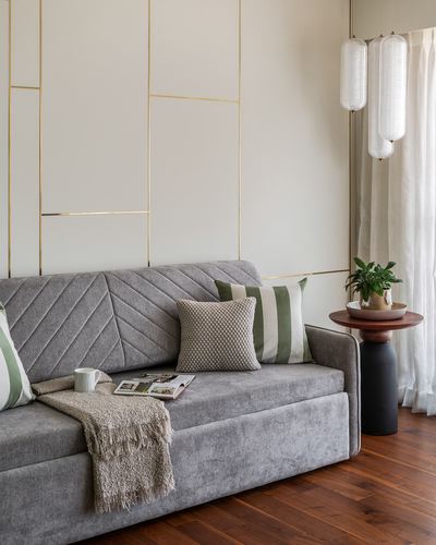 Grey quilted sofa with cushions and throw against brass-lined panelled wall, pendant lights beside.