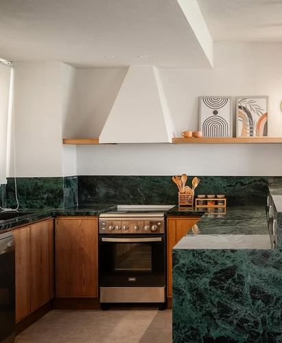 Kitchen corner with green stone counters, wood cabinets, sculptural white hood and open shelf