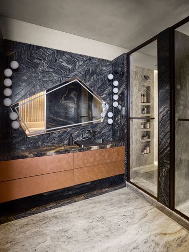Bathroom with dark veined marble walls, copper floating vanity, and hexagonal mirror flanked by globe lights
