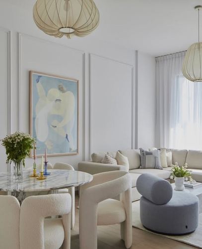 Open living-dining space with cream bouclé chairs, marble table, and pale blue figurative painting