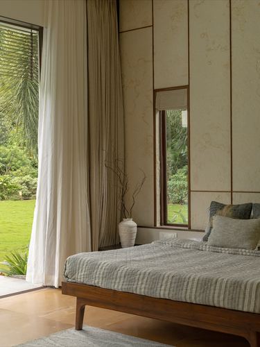 Bedroom with wood-framed bed, textured stone wall panels, and a slit window overlooking a garden