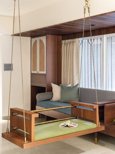 Wooden hanging swing with green cushion in front of a sofa nook with wood-panelled ceiling and cane cabinet