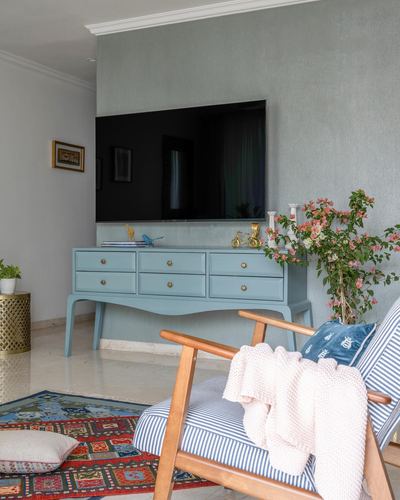 Living room with blue console under wall tv, striped armchair, bougainvillea and patterned rug