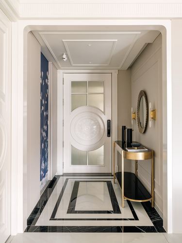 Entryway with carved white door, marble medallion floor, brass console table and oval mirror
