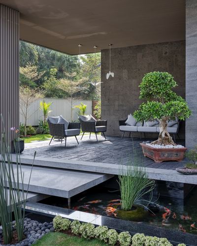 Outdoor lounge deck with cane chairs, bonsai tree, and koi pond beneath a covered terrace