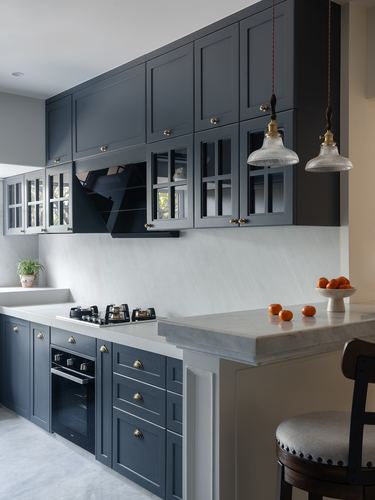 Navy shaker kitchen with marble countertop, glass-front cabinets, and two glass pendant lights over a peninsula