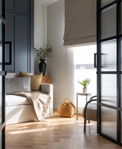 Living room corner with white sofa, dark cabinetry, herringbone floor, and black-framed glass door.