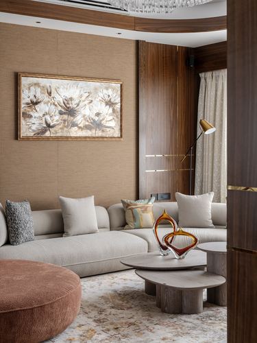 Curved beige sofa with glass sculptures on nested coffee tables beside a textured tan wall.