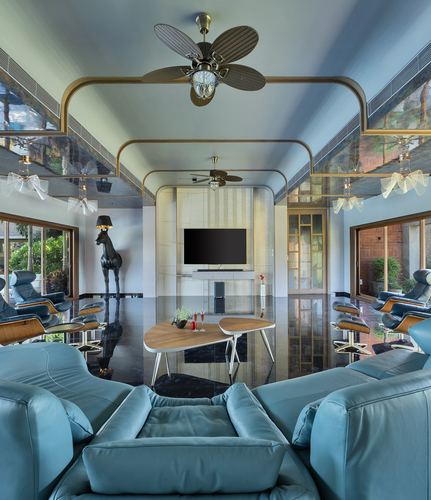 Long symmetrical living room with teal leather sofas, brass ceiling frames, and a black horse sculpture.