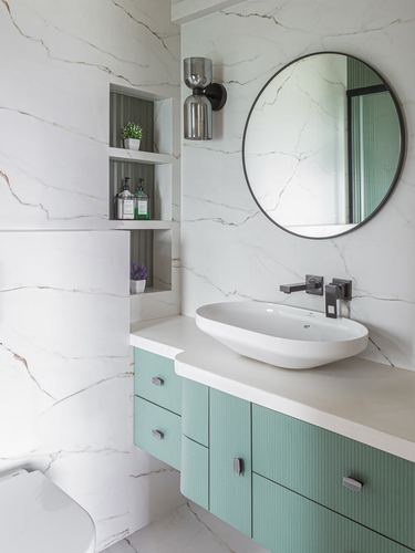 Bathroom with veined stone walls, round black-framed mirror, and sage green fluted vanity with vessel sink