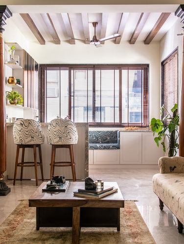 Living room with exposed wood beams, patterned bar stools, window seat, and a carved wooden pillar
