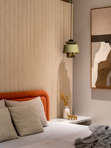 Bedroom corner with orange headboard, fluted beige wall, and green pendant light over marble nightstand