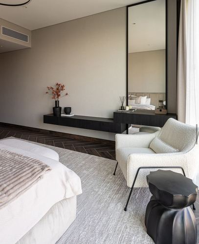 Modern bedroom with floating console, tall mirror, and boucle armchair on textured rug