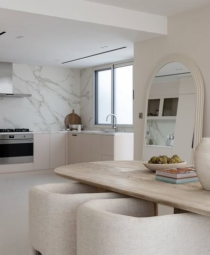 Open kitchen with marble backsplash, arched mirror, and curved beige chairs at a wooden table