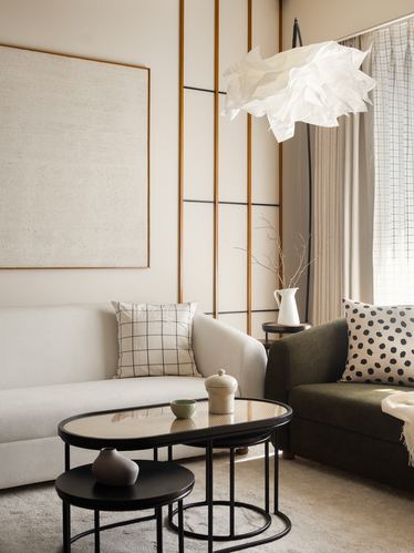 Neutral living room with white and olive sofas, nesting cane-top coffee tables, and a cloud-shaped paper pendant light