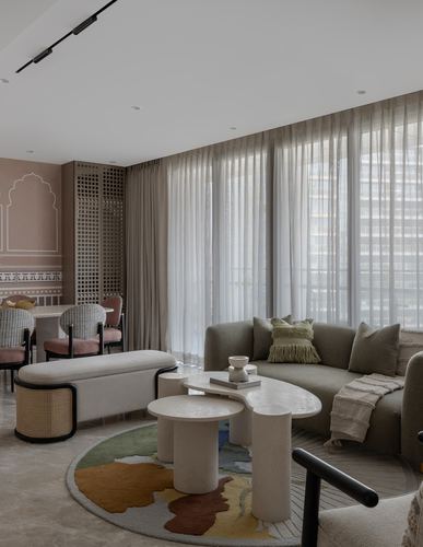 Living room with olive sofa, round rug, sculptural stone tables, and cane bench near a jali screen partition