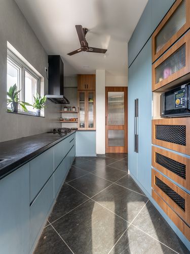 Galley kitchen with blue cabinetry, dark stone counters, wood cane-front units, and a ceiling fan