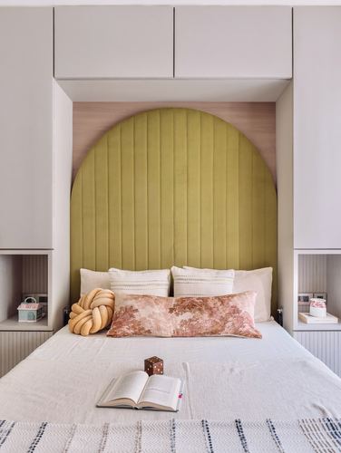 Bed with arched olive velvet headboard flanked by built-in cabinetry and open cubbies