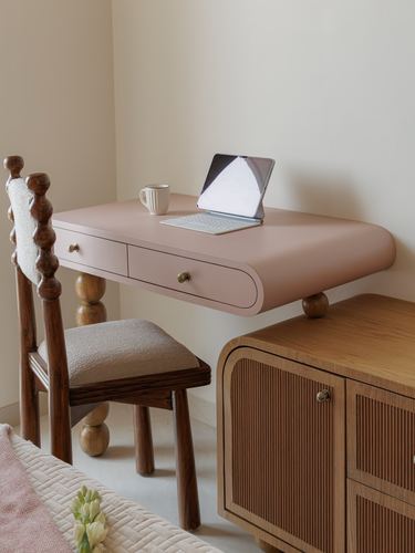 Pink wall-mounted desk with turned wooden chair beside ribbed oak cabinet